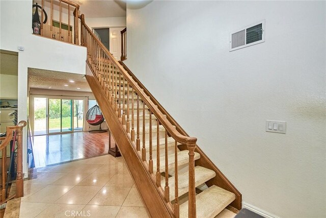 staircase with a towering ceiling, tile patterned floors, and visible vents