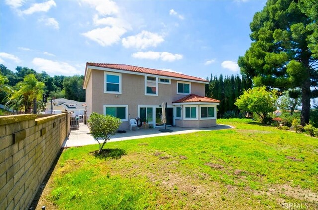 back of house featuring fence, stucco siding, a patio area, a lawn, and a tiled roof