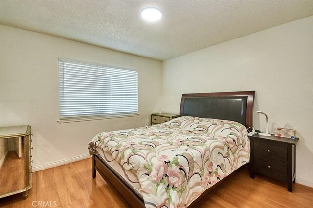 bedroom featuring a textured ceiling, baseboards, and wood finished floors