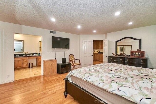 bedroom with a textured ceiling, visible vents, light wood finished floors, connected bathroom, and recessed lighting