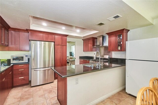 kitchen featuring visible vents, wall chimney range hood, a tray ceiling, and white appliances