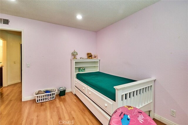 bedroom with a textured ceiling, recessed lighting, baseboards, wood finished floors, and visible vents