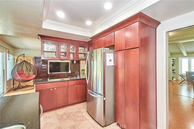 kitchen with freestanding refrigerator, ornamental molding, dark countertops, glass insert cabinets, and a sink