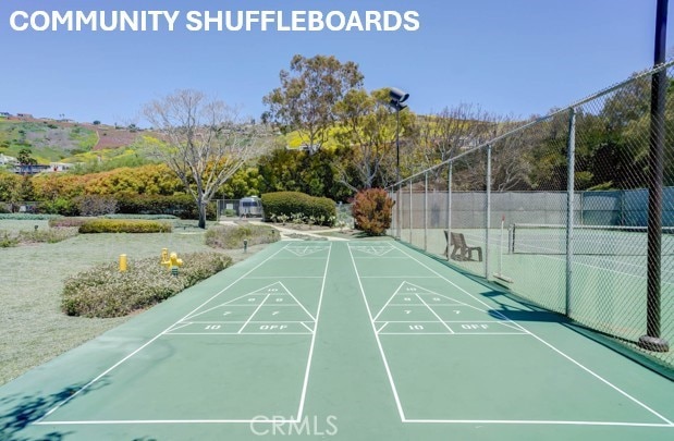 view of community with fence, a tennis court, and shuffleboard