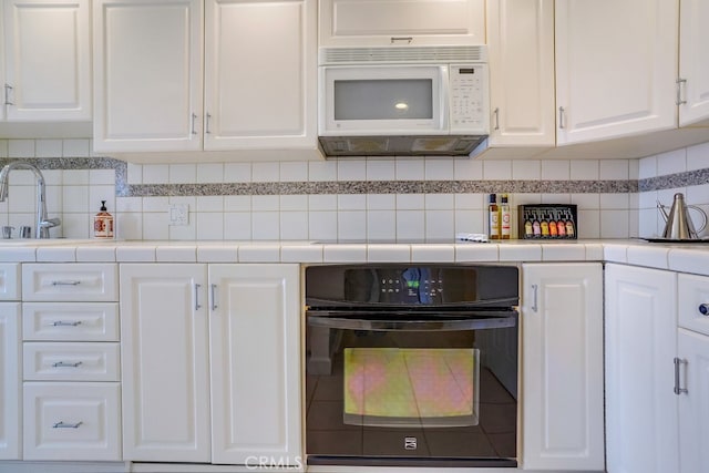 kitchen featuring white cabinets, oven, tile countertops, white microwave, and backsplash
