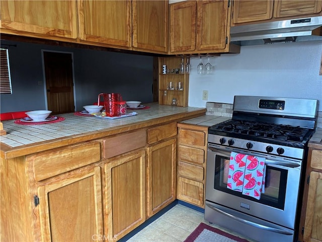 kitchen featuring tile countertops, brown cabinets, stainless steel gas stove, and under cabinet range hood