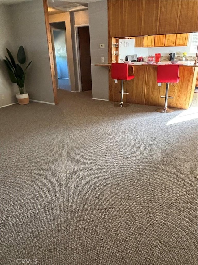 kitchen with brown cabinets, a breakfast bar, a peninsula, light countertops, and carpet floors