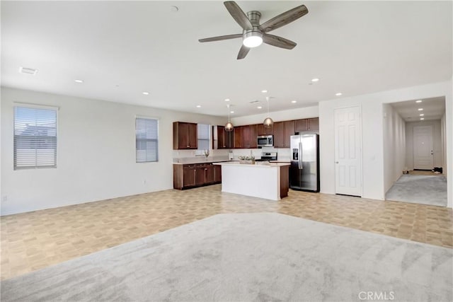 kitchen with ceiling fan, a center island, light countertops, open floor plan, and stainless steel appliances