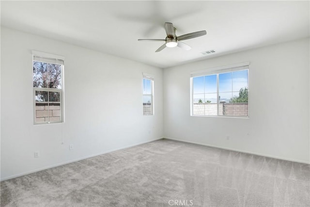 carpeted empty room with baseboards, a ceiling fan, and visible vents