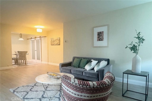 living room with a barn door, wood finished floors, and baseboards