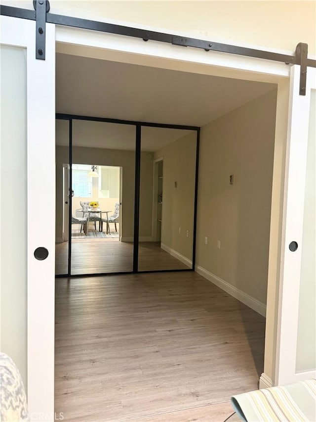 interior space with light wood finished floors, a barn door, and baseboards
