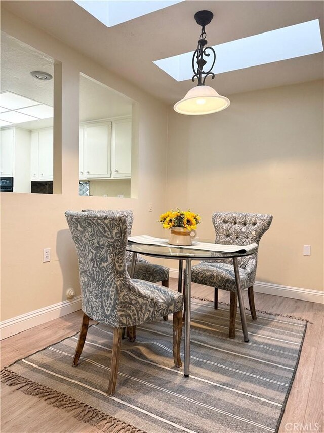 dining room with baseboards, a skylight, and light wood finished floors