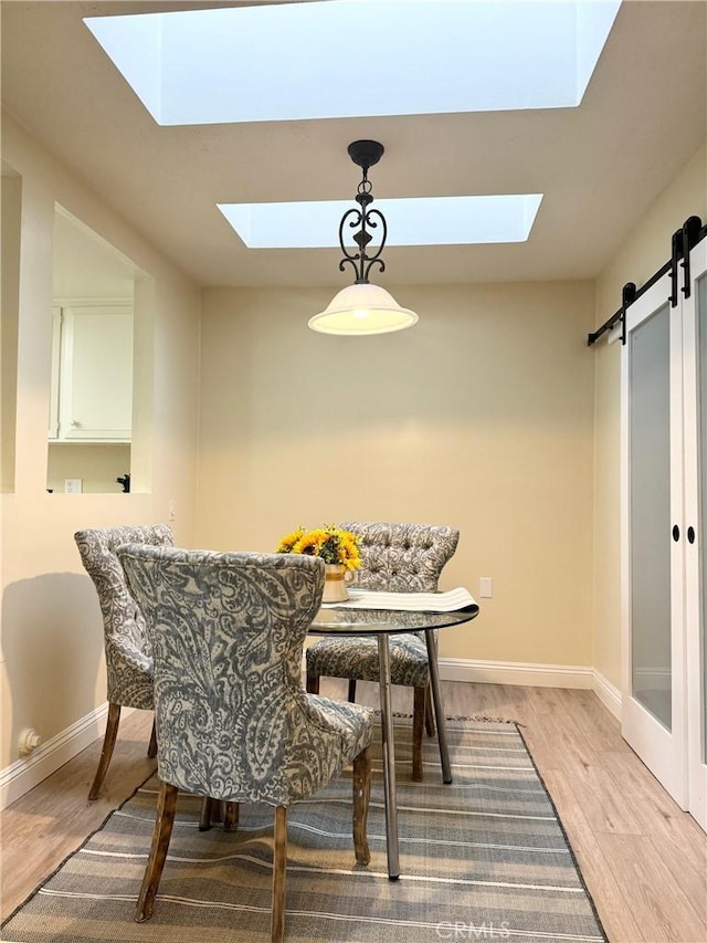 dining space with baseboards, a barn door, a skylight, and light wood-style flooring
