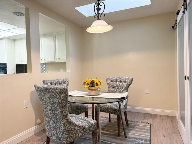 dining area with a barn door, baseboards, light wood finished floors, and a skylight