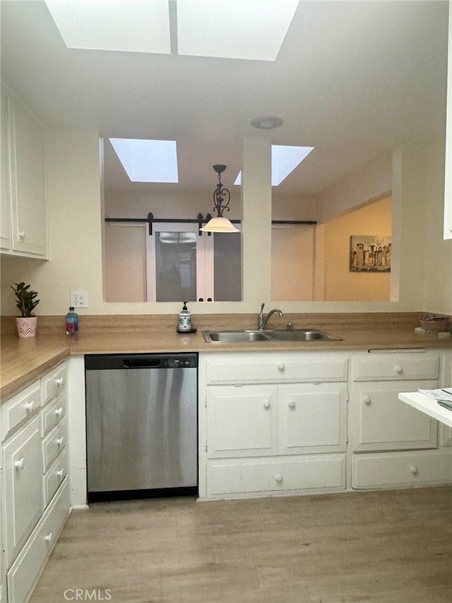 kitchen featuring stainless steel dishwasher, white cabinets, light wood-style flooring, a sink, and a skylight