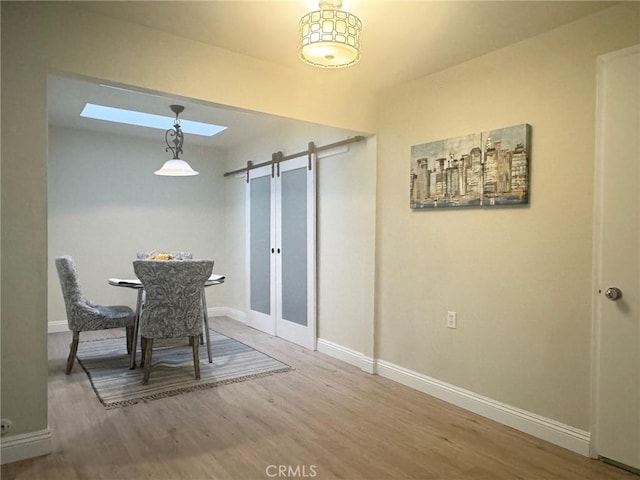 dining space featuring a skylight, wood finished floors, baseboards, and a barn door