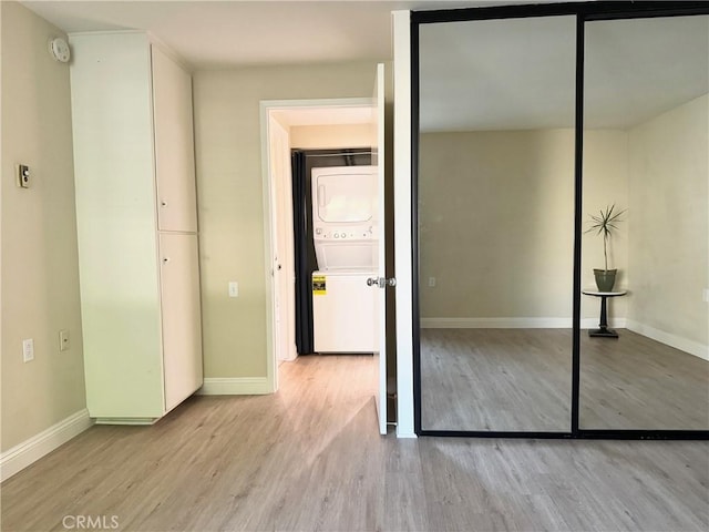 unfurnished bedroom featuring baseboards, wood finished floors, stacked washer / drying machine, and a closet