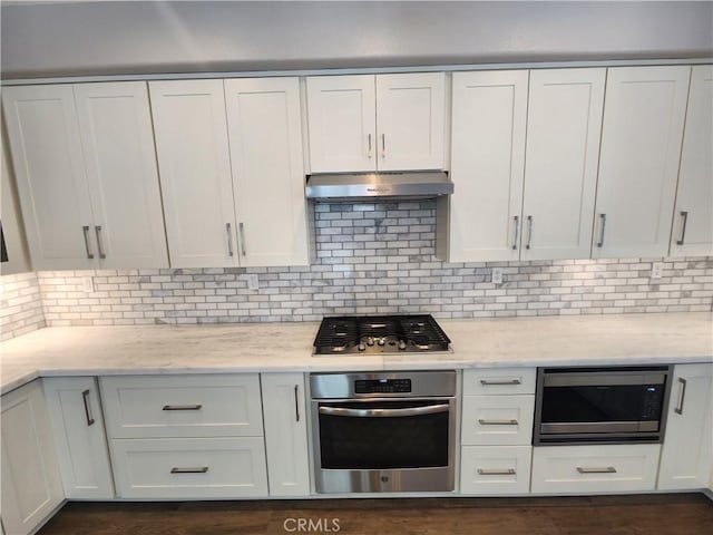 kitchen featuring white cabinetry, tasteful backsplash, stainless steel appliances, under cabinet range hood, and light stone countertops