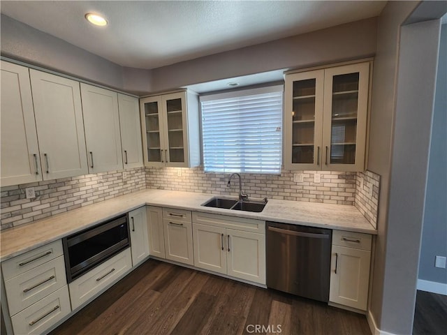 kitchen featuring decorative backsplash, stainless steel appliances, white cabinets, a sink, and dark wood-style floors