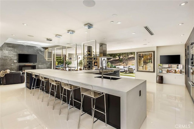 kitchen with a large island with sink, island exhaust hood, pendant lighting, open floor plan, and a kitchen breakfast bar