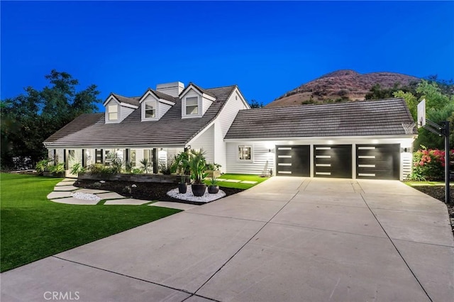 new england style home featuring a chimney, driveway, a mountain view, a front lawn, and an attached garage