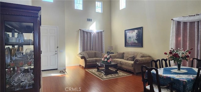 living room with baseboards, visible vents, wood finished floors, and a towering ceiling