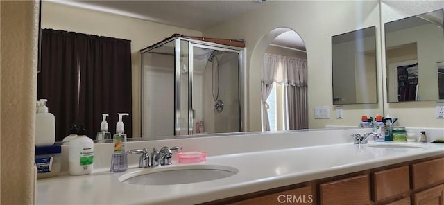 bathroom with a shower stall, double vanity, and a sink