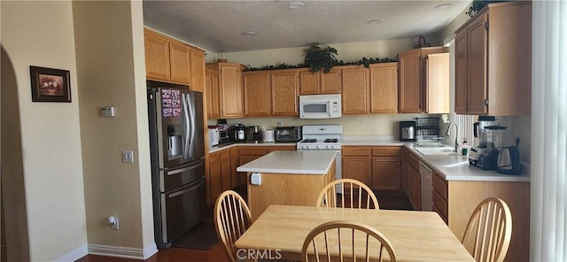 kitchen featuring white appliances, light countertops, a sink, baseboards, and a center island