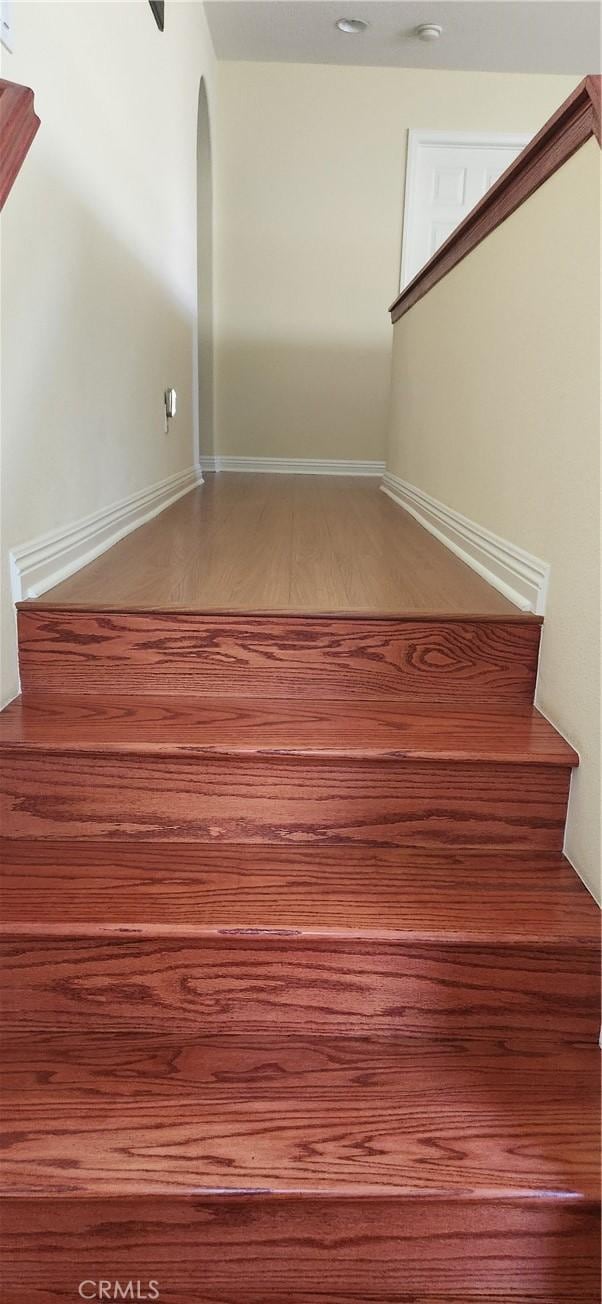 staircase with baseboards, arched walkways, and wood finished floors