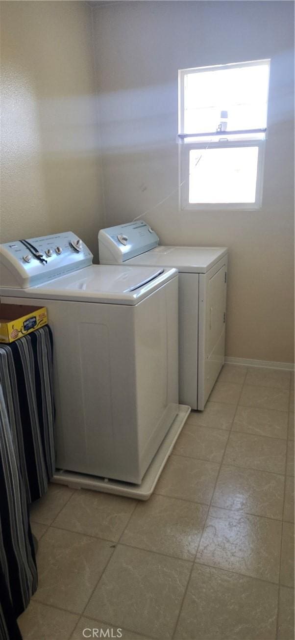 laundry room featuring baseboards, light tile patterned floors, separate washer and dryer, and laundry area