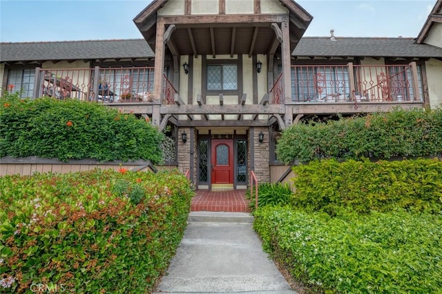 view of front of property with roof with shingles, stucco siding, and a balcony