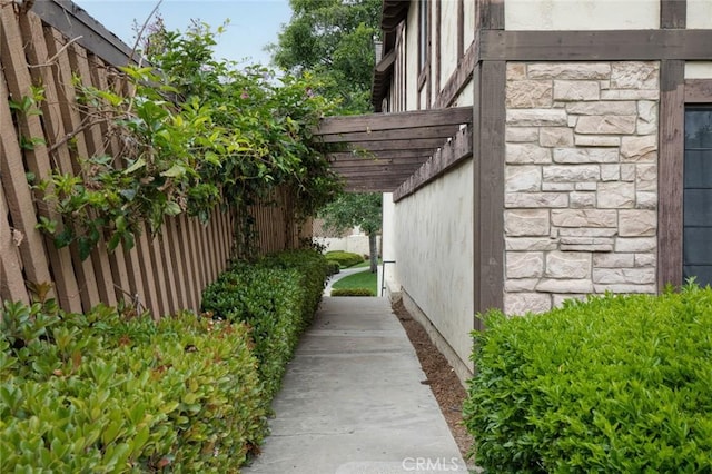 view of property exterior featuring fence, a pergola, and stone siding