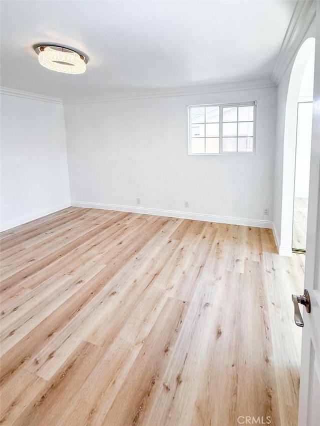 spare room with baseboards, arched walkways, wood finished floors, and ornamental molding