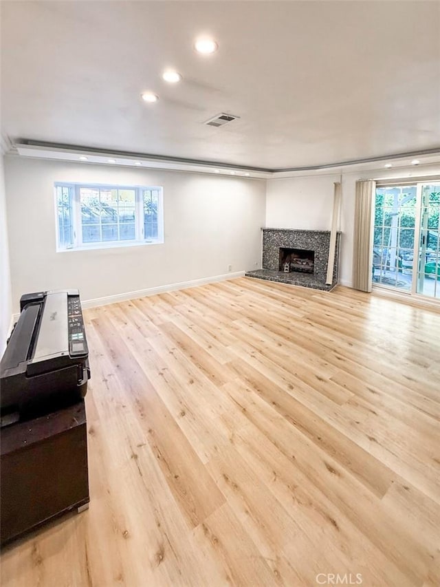 unfurnished living room featuring recessed lighting, wood finished floors, a fireplace with raised hearth, baseboards, and visible vents