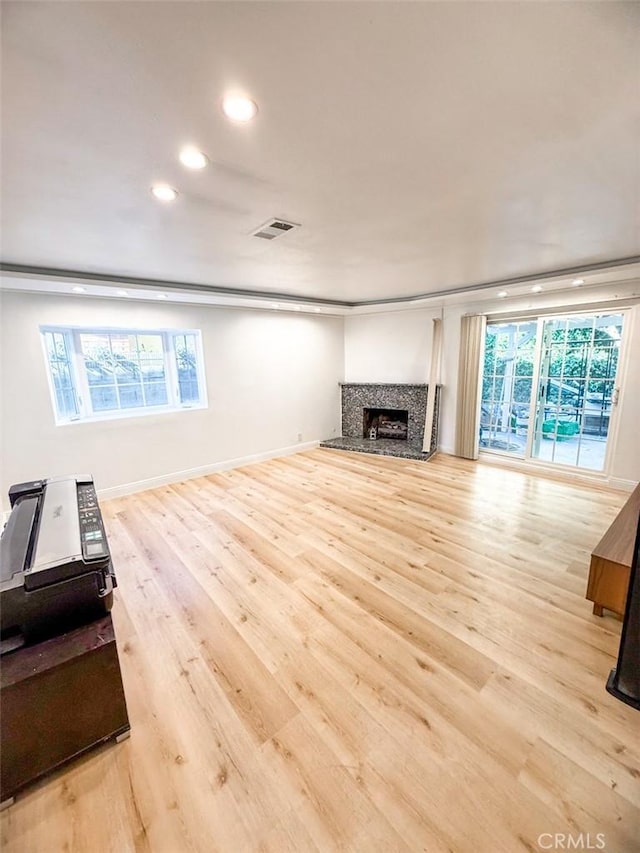 unfurnished living room featuring visible vents, a fireplace with raised hearth, baseboards, recessed lighting, and light wood finished floors