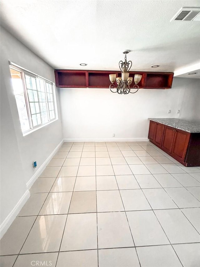 unfurnished dining area with light tile patterned floors, a textured ceiling, visible vents, baseboards, and a notable chandelier