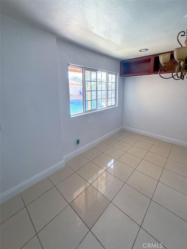 empty room featuring a textured ceiling, light tile patterned floors, and baseboards