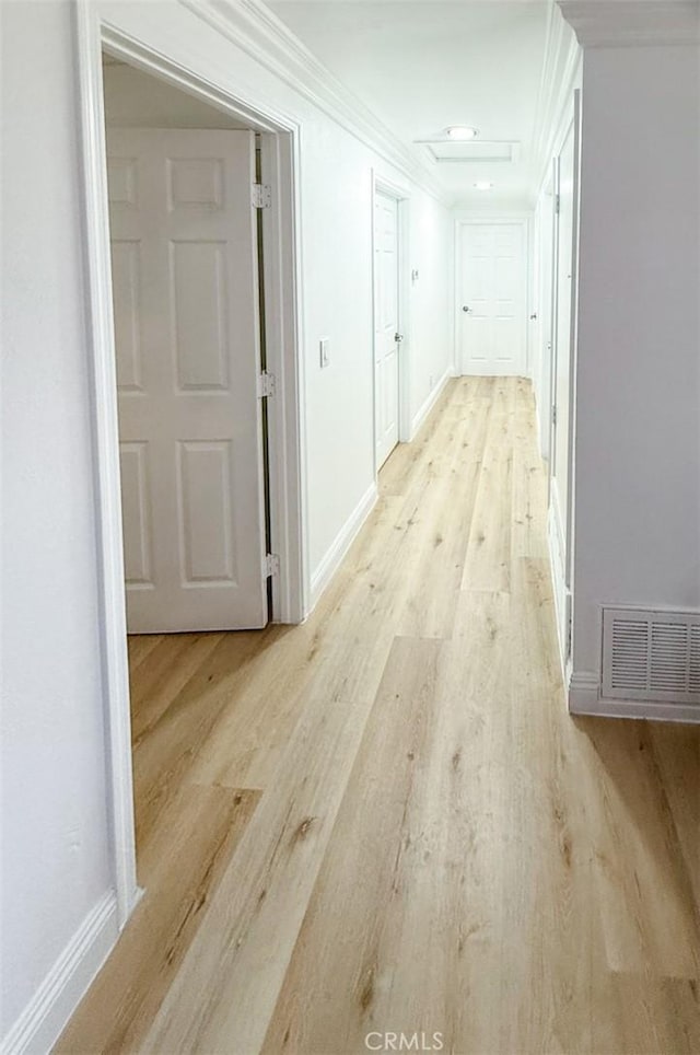 hall featuring attic access, light wood finished floors, visible vents, baseboards, and ornamental molding