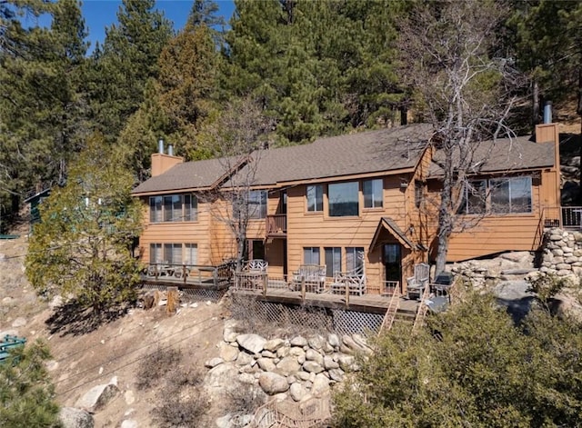 rear view of house with a chimney, a wooden deck, and a balcony