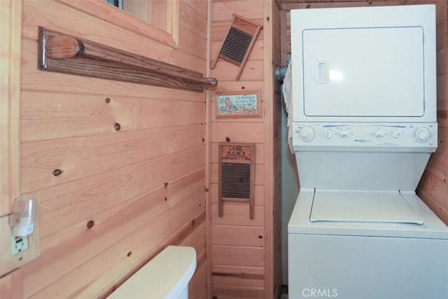 laundry area with stacked washer / dryer, wood walls, and laundry area