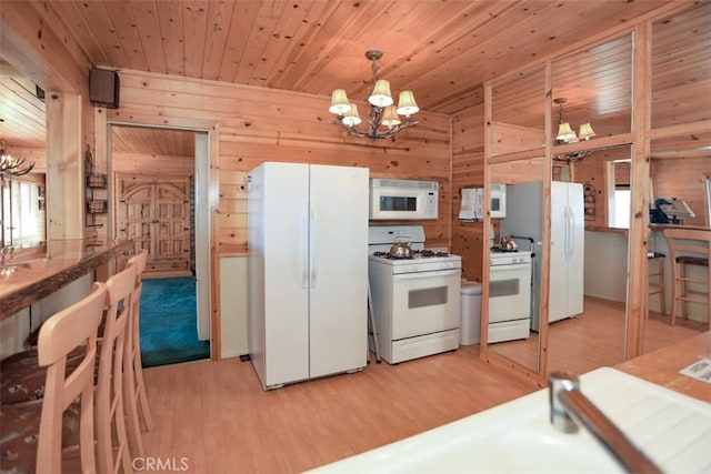 kitchen featuring light wood-style floors, an inviting chandelier, wood walls, and white appliances