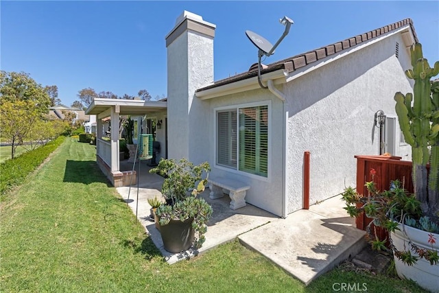 rear view of house with a patio, a yard, stucco siding, and a chimney