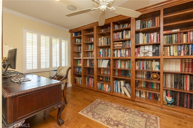 office area with crown molding, wall of books, ceiling fan, and wood finished floors