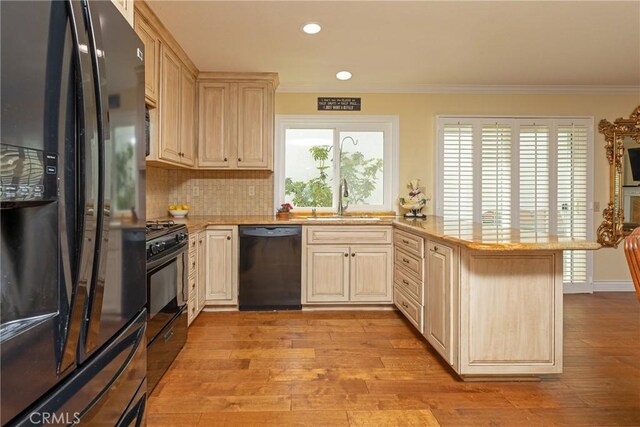 kitchen featuring black appliances, light wood finished floors, a sink, a peninsula, and crown molding