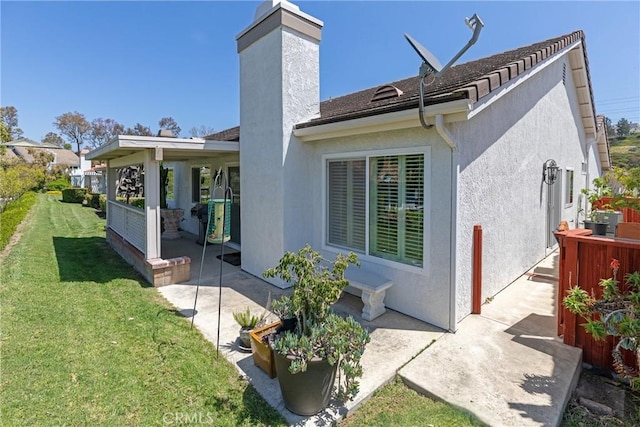back of house with stucco siding, a chimney, a yard, and a patio area