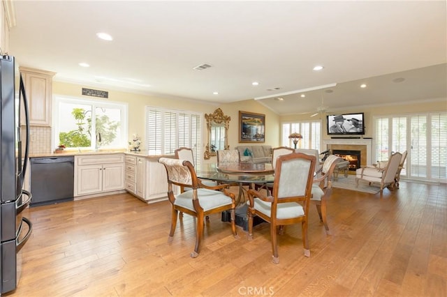 dining room featuring vaulted ceiling, ceiling fan, light wood finished floors, a glass covered fireplace, and visible vents