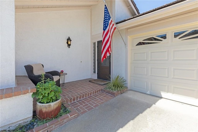 doorway to property featuring concrete driveway, a garage, and stucco siding