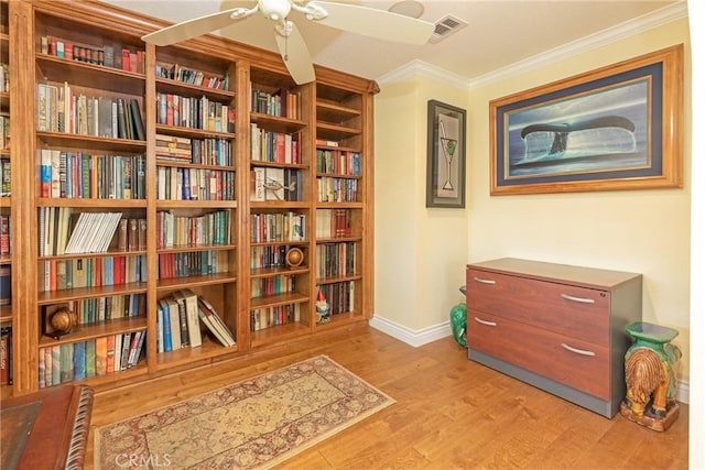 living area featuring wood finished floors, bookshelves, baseboards, visible vents, and crown molding