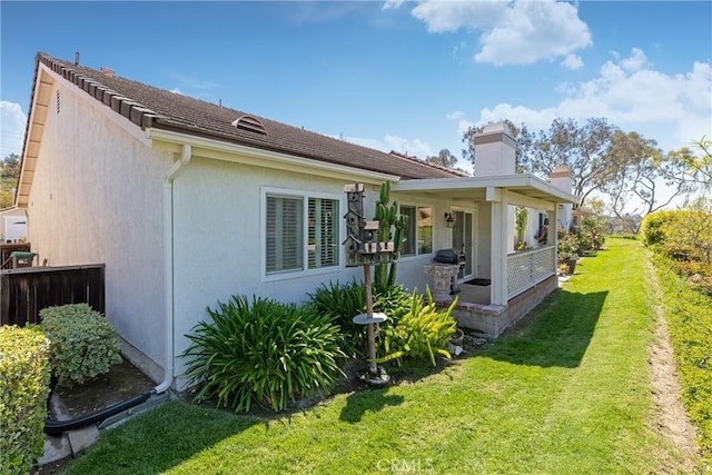 rear view of property with stucco siding, fence, a chimney, and a yard