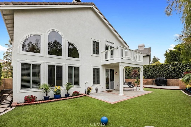 back of property with a lawn, a balcony, a fenced backyard, a patio, and stucco siding